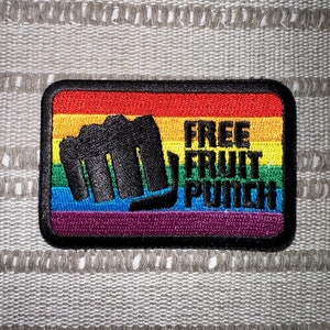 以下が含まれることがあります： 虹色の刺繍パッチで、黒い拳と「FREE FRUIT PUNCH」の文字が書かれています。