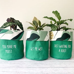 May include: Three green fabric plant pots with white and green leaf patterns. The pots have different sayings on them: "You make me moist", "Get me wet", and "Just waiting for a root".