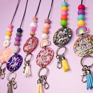 May include: A set of six colourful beaded lanyards with personalised name tags. Each lanyard features a rainbow charm and a tassel. The name tags are made of clear resin with glitter and confetti.