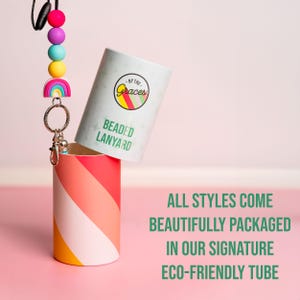 May include: A colorful beaded lanyard with a rainbow charm and a silver key ring. The lanyard is packaged in a white tube with the text "By The Graces" and "Beaded Lanyard" printed on it. All styles come beautifully packaged in our signature eco-friendly tube.