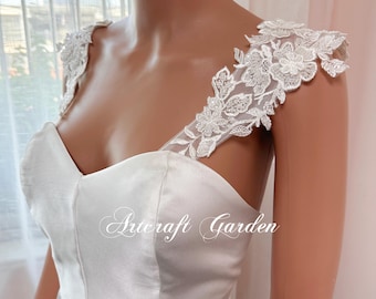 May include: White satin strapless wedding dress with delicate lace straps. The straps are adorned with floral lace appliques.