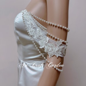 May include: A white satin dress with a pearl and lace embellishment on the shoulder. The lace features a floral design.