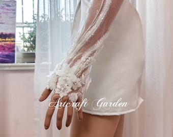 Puede incluir: Guantes de encaje blanco con adornos florales y tela transparente. Los guantes se llevan en la mano de un maniquí. El texto "Artcraft Garden" es visible en la imagen.