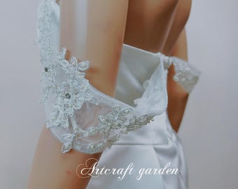Puede incluir: Un vestido de novia blanco de hombros descubiertos con delicados detalles de encaje en las mangas. El vestido tiene un corpiño ajustado y una falda fluida.