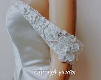 May include: A white satin wedding dress with a delicate floral lace trim on the shoulder straps. The lace features small white flowers and pearls.