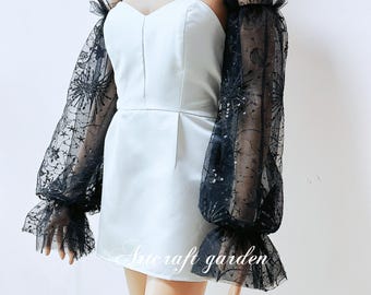 May include: A white strapless dress with black sheer lace sleeves. The sleeves have a delicate floral pattern and are adorned with sequins. The dress is short and has a fitted bodice.