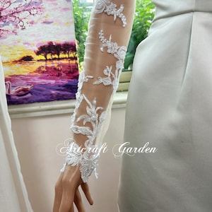May include: A sheer white sleeve with intricate floral lace detailing. The lace features delicate, raised floral patterns with subtle beadwork. The text "Artcraft Garden" is printed on the sleeve.