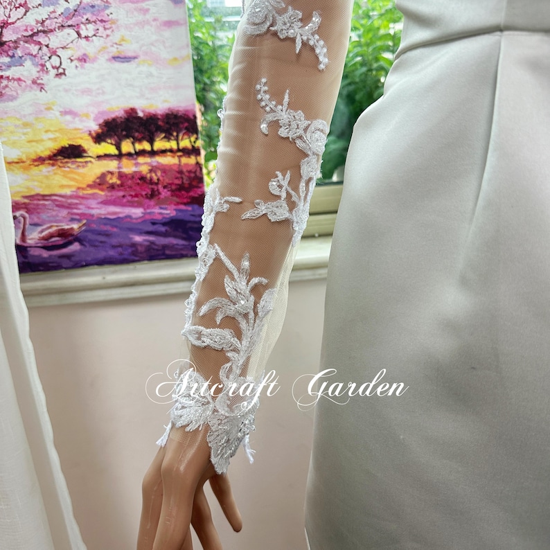May include: A sheer white sleeve with intricate floral lace detailing. The lace features delicate, raised floral patterns with subtle beadwork. The text "Artcraft Garden" is printed on the sleeve.