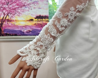 May include: White bridal gloves with intricate floral lace and bead embellishments. The sheer sleeves feature delicate patterns and the text "Artcraft Garden". Perfect for weddings or special occasions.