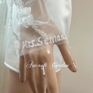 May include: White bridal veil with delicate floral and beaded embellishments. The veil features the embroidered text "Mrs. Sema" and the brand name "Artcraft Garden". The design includes a sheer, layered fabric.