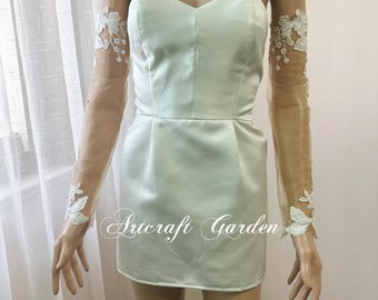 Puede incluir: Un minivestido de satén verde claro con escote corazón. El vestido tiene un corpiño ajustado y una falda corta. Mangas largas transparentes con detalles de encaje floral blanco están adjuntas. El texto "Artcraft Garden" está impreso en el vestido.