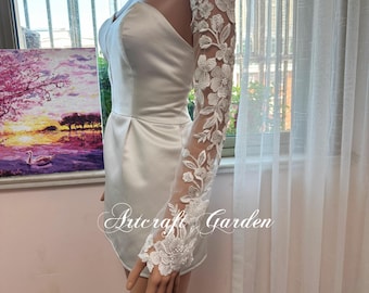 May include: White satin romper with a sweetheart neckline and a delicate floral lace sleeve. The lace sleeve features intricate floral and leaf patterns. The text "Artcraft Garden" is visible on the garment.