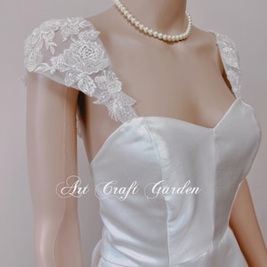 Könnte beinhalten: Ein weißes Satin-Hochzeitskleid mit einem herzförmigen Ausschnitt und Spitzenträgern. Das Kleid hat ein tailliertes Oberteil und einen fließenden Rock. Der Text "Art Craft Garden" ist auf dem Kleid sichtbar.