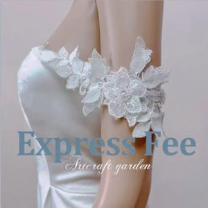 May include: A white floral lace arm cuff with a sequined flower design. The cuff is adorned with delicate leaves and is worn on the upper arm. The text "Express Fee" and "Artcraft garden" are visible in the image.