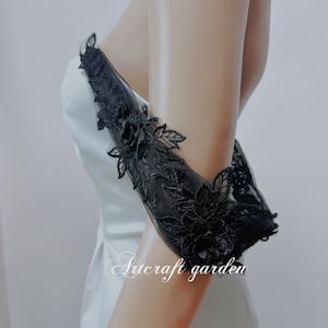 May include: Black lace applique with floral details on a white dress. The lace is delicate and features a variety of floral designs. The dress is a simple, elegant style.