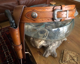 Peut inclure: Une ceinture à pistolet en cuir marron avec une boucle argentée et un holster assorti. La ceinture est ornée d'un motif en forme d'étoile et le holster est décoré de surpiqûres.