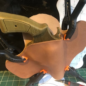 May include: A brown leather holster is being clamped to a green 3D printed gun. The holster is being held in place by several clamps.