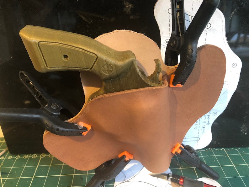 May include: A brown leather holster is being clamped to a green 3D printed gun. The holster is being held in place by several clamps.