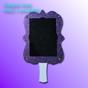 May include: A purple glitter-covered chalkboard with a decorative frame and a white handle. The text "Unique item. Only 1 available" is in the upper left corner. The chalkboard has a black center.