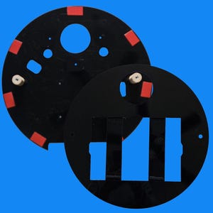 May include: Two black circular watch faces with red and white accents, and blue cutouts. One face is partially overlapping the other, revealing the design details. The background is a solid blue.
