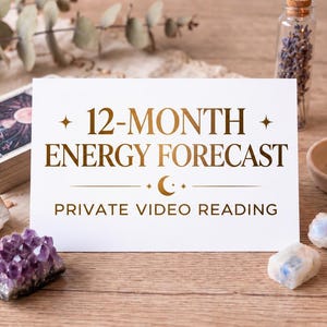 May include: A white rectangular card with gold text reading 12-MONTH ENERGY FORECAST PRIVATE VIDEO READING, surrounded by a deck of tarot cards, a lit yellow beeswax candle in a ceramic holder, a small glass vial of dried lavender, and crystals.