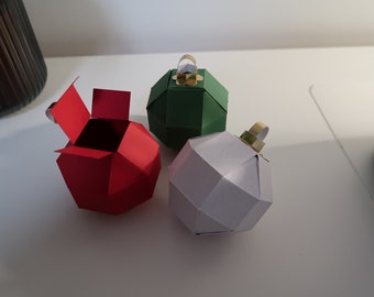 Op de afbeelding: Drie papieren kerstversieringsdozen, een rode, een groene en een witte. De rode doos is open en laat een lege binnenkant zien.