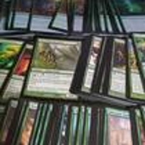 May include: A collection of rectangular trading cards arranged in overlapping rows. The cards feature green borders and various illustrations, including a central card depicting a creature in a forest setting. Text is visible on the card faces.