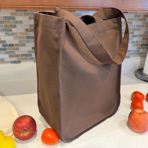 May include: A brown canvas tote bag with two handles. The bag is sitting on a white countertop with some red apples and tomatoes.