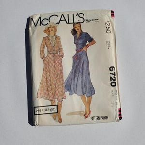 May include: A vintage McCall's sewing pattern with illustrations of two dresses. The envelope is off-white, with the text "McCall's" and "6720". The illustrations show a plaid dress and a blue dress, with the price in dollars.