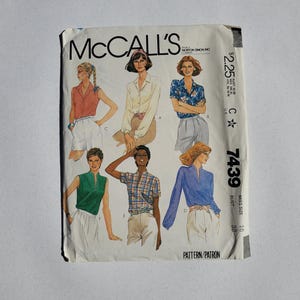 May include: Vintage McCall's sewing pattern featuring illustrations of blouses and shorts. The pattern cover displays various blouse styles in different colors and patterns. The text "McCall's" is at the top, with the pattern number 7439 and price.