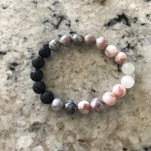 May include: A bracelet made of black lava rock beads, grey and pink marbled beads, and white beads.