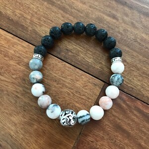 May include: A black lava rock and white and pink marbled stone beaded bracelet with a silver charm.