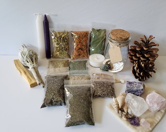 May include: An assortment of spiritual items, including dried herbs in clear bags, candles, crystals, a pine cone, and a small glass jar with a cork lid. The items are arranged on a white surface.