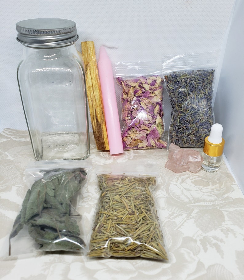 May include: A collection of items for a ritual or spell, including a clear glass bottle with a silver lid, a pink candle, a wooden stick of incense, a bag of dried rose petals, a bag of dried lavender, a small bag of dried herbs, a bag of dried rosemary, a pink crystal, and a small bottle of oil.