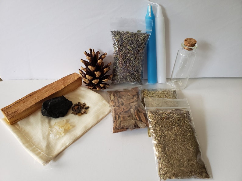 May include: A collection of items for a cleansing ritual, including a white candle, a small bottle, a pine cone, a bag of lavender, a bag of herbs, a bag of cinnamon sticks, a bag of dried herbs, a piece of palo santo wood, a black stone, and a small bag of crystals.