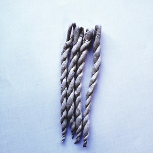 May include: Five gray braided incense sticks on a white background.
