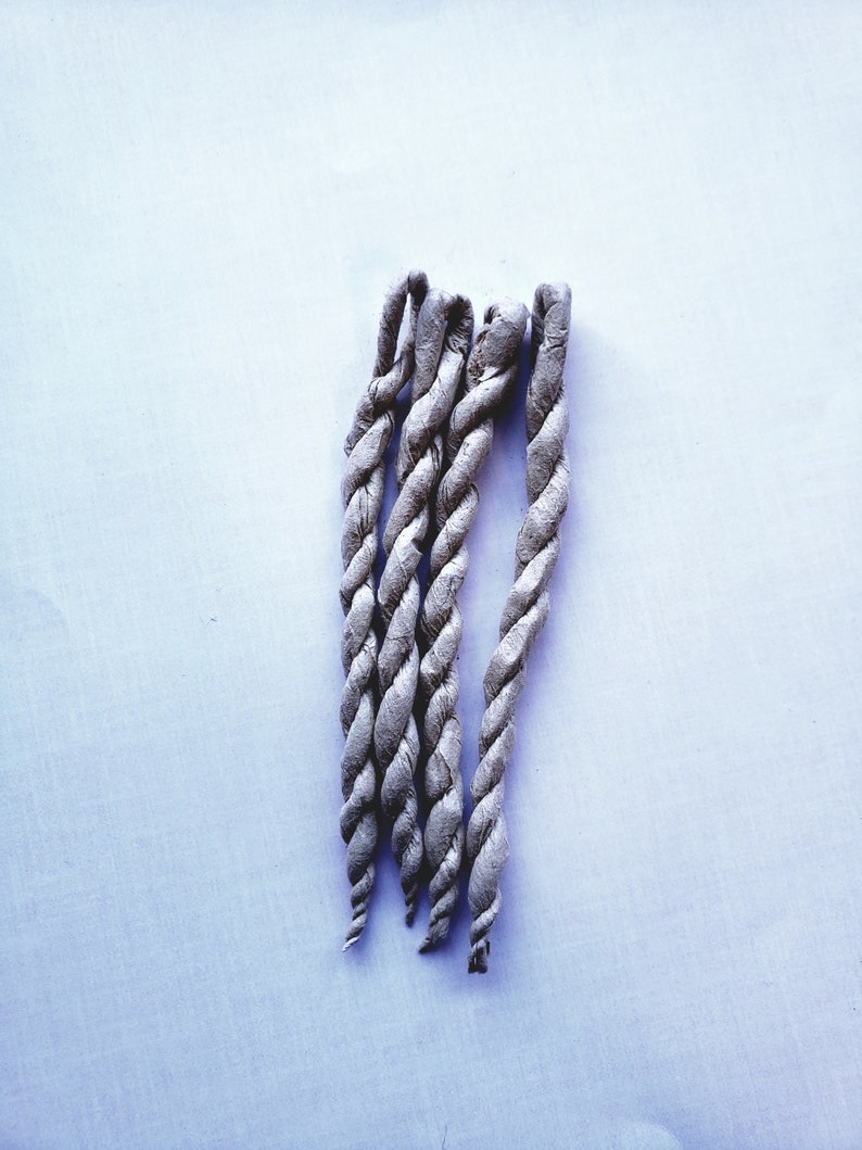 May include: Five gray braided incense sticks on a white background.