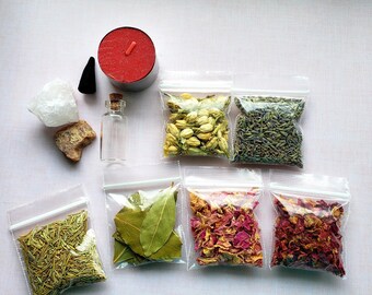 May include: A collection of dried herbs and flowers in small clear plastic bags, including rosemary, bay leaves, jasmine, lavender, rose petals, and red rose petals. There is also a small clear glass bottle, a white crystal, a red candle, and a black incense cone.