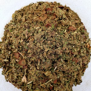 May include: A close-up of a pile of dried herbs and flowers, including green leaves, brown stems, and red berries. The mixture appears to be a blend of various botanicals, likely for use in herbal teas or other medicinal purposes.