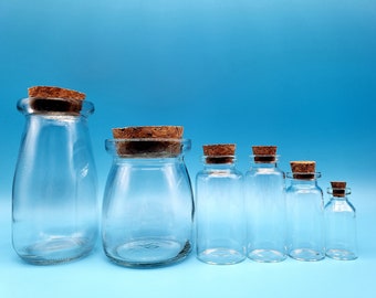 May include: A set of seven clear glass bottles with cork stoppers. The bottles are of varying sizes, with the largest bottle being a rounded shape and the smaller bottles being rectangular. The bottles are arranged in a row from largest to smallest, with the largest bottle on the left and the smallest bottle on the right.