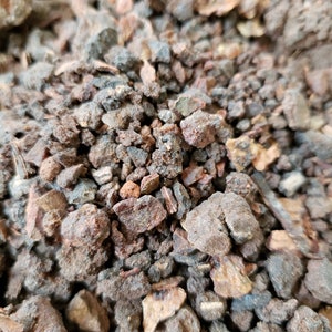 May include: Close-up of a pile of dark brown and reddish-brown resinous pieces. The pieces are irregular in shape and size, with some being quite small and others being larger.