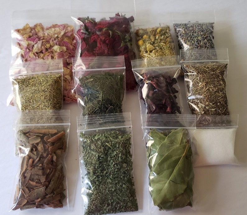 May include: Twelve clear plastic bags filled with various dried herbs and flowers. The bags are arranged in three rows of four. The herbs and flowers include rose petals, lavender, rosemary, bay leaves, and other unidentified herbs.