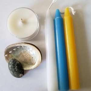 May include: A white, blue, and yellow candle set with a small white tea light candle and a seashell.