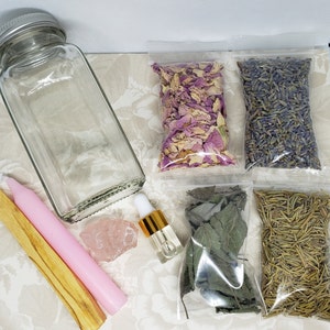 May include: A glass jar, pink candle, wooden stick, rose quartz crystal, and four small bags containing dried herbs and flowers. The bags contain dried rose petals, lavender, sage, and rosemary.