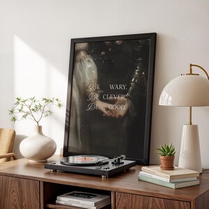 Puede incluir: Una impresi&oacute;n enmarcada con el texto "Be wary. Be clever. Be good." est&aacute; sobre un mueble de madera. Un tocadiscos est&aacute; frente a la impresi&oacute;n. Una l&aacute;mpara blanca y una peque&ntilde;a planta en maceta est&aacute;n sobre el mueble.