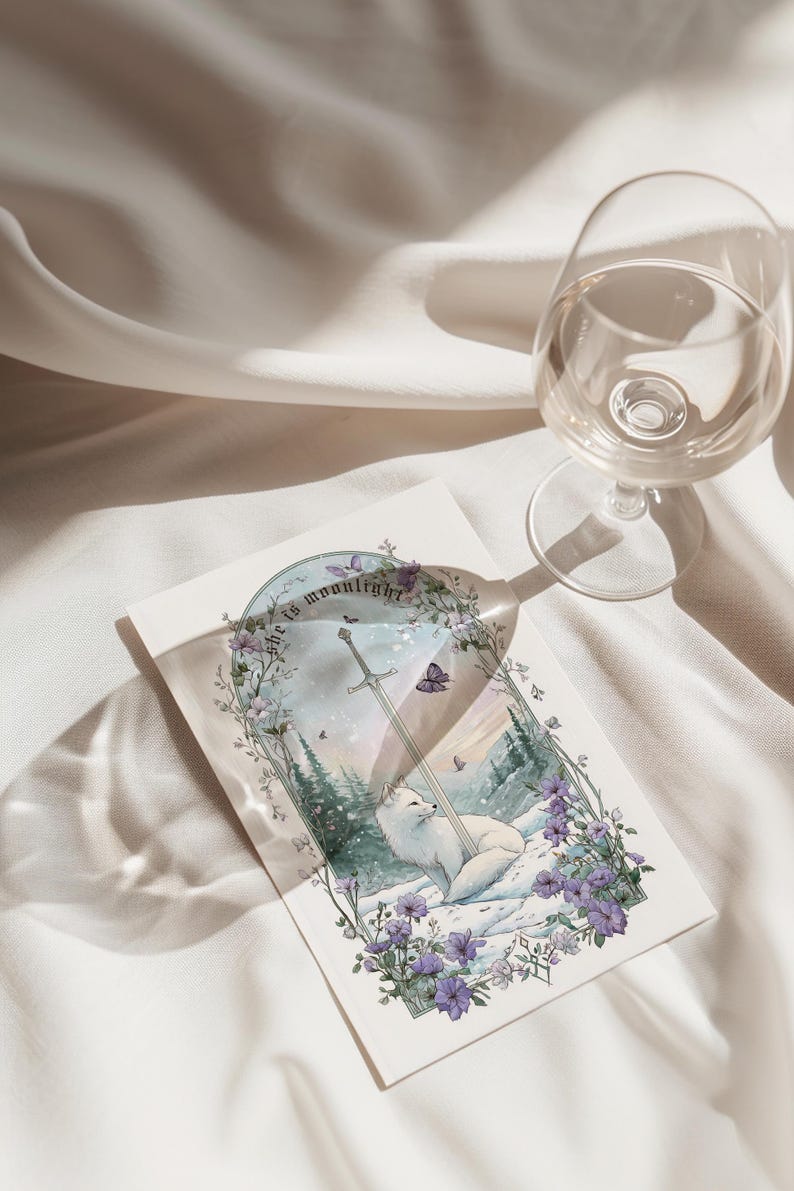 Puede incluir: Una tarjeta de felicitaci&oacute;n con un zorro blanco descansando en un paisaje nevado con una espada y el texto "she is moonlight". La tarjeta est&aacute; rodeada de flores moradas y mariposas. Una copa de vino est&aacute; en el fondo.