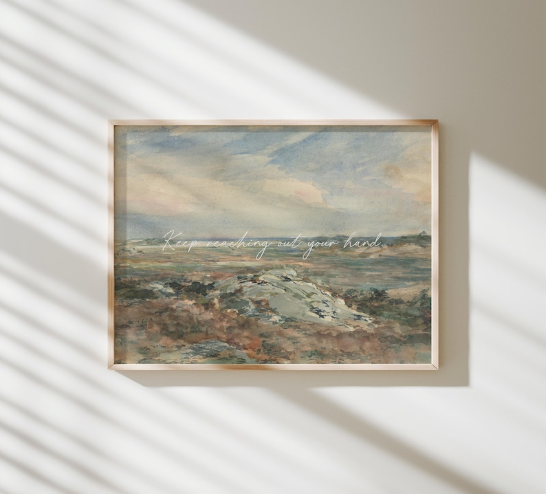 May include: A framed landscape art print. The artwork depicts a muted color palette of blues, greens, and browns, with a cloudy sky and a rocky terrain. The print has a wooden frame and the words 'Keep reaching out your hand' are written in a delicate font.
