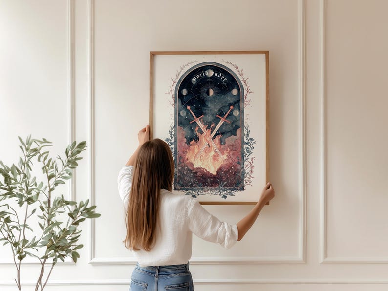 Puede incluir: Una impresi&oacute;n art&iacute;stica enmarcada con una ilustraci&oacute;n de acuarela de tem&aacute;tica celestial. La obra de arte representa espadas cruzadas sobre llamas, con las palabras "world under" en la parte superior. La impresi&oacute;n es sostenida por una persona.