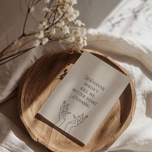 May include: A wooden tray holds a card with the text "Whatever doesn't kill me, better start running." The card features a line drawing of hands. Dried flowers and a white cloth complete the scene.