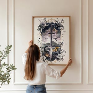 以下が含まれることがあります： 剣、ドラゴン、そして「great little thing」というテキストが描かれたファンタジーシーンの額入りアートプリント。 アートワークは花の要素に囲まれ、曇り空を背景に設定されています。 フレームは明るい茶色です。